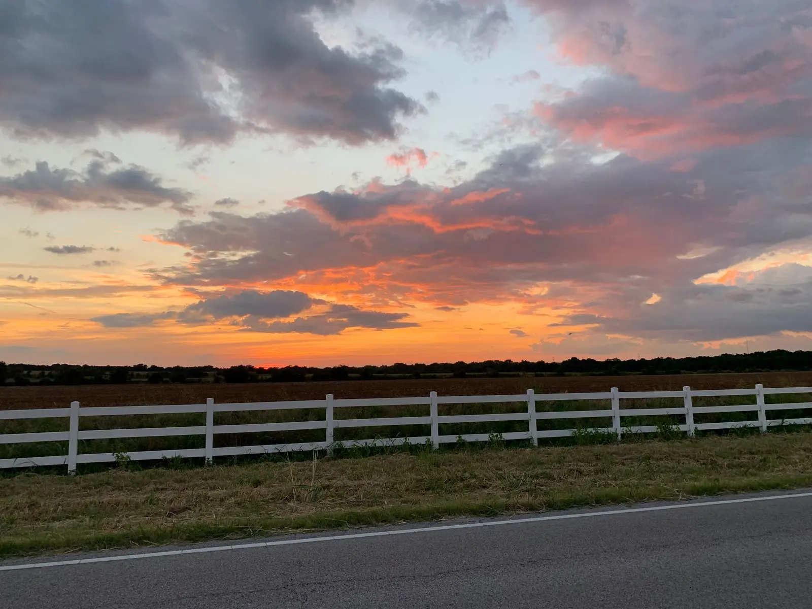 Sunset over a Texas pasture with a white fence along the road